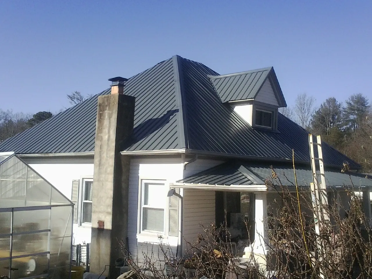 Dark blue standing seam metal roof on a white farmhouse with dormer — Slate & Tile Roof Repair by Roofing Brothers in Brockton