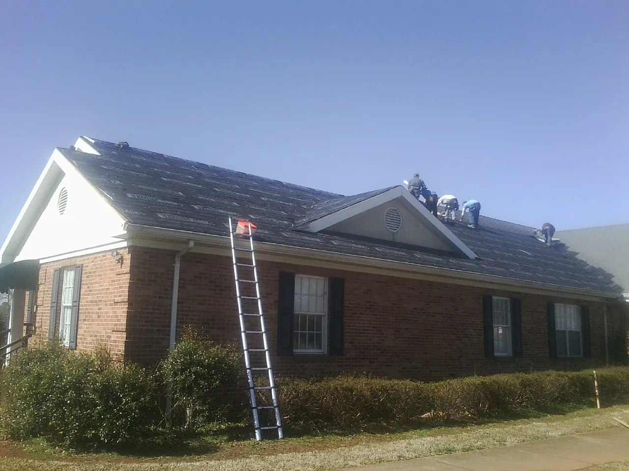 Crew tearing shingles off a brick ranch roof with a ladder set — Emergency Roof Repair work by our crew in Brockton