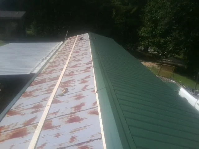 Old rusted panels beside newly installed green metal roofing — Wind Damage Roof Repair by Roofing Brothers in Brockton