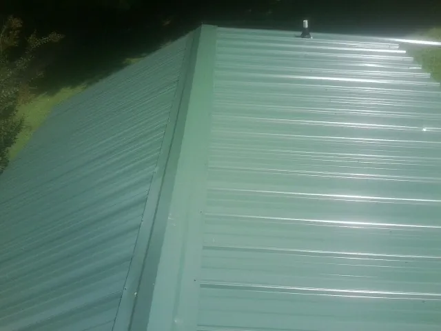 New green metal panels meeting at the ridge of a roof — Flat Roof Repair work by our crew in Brockton