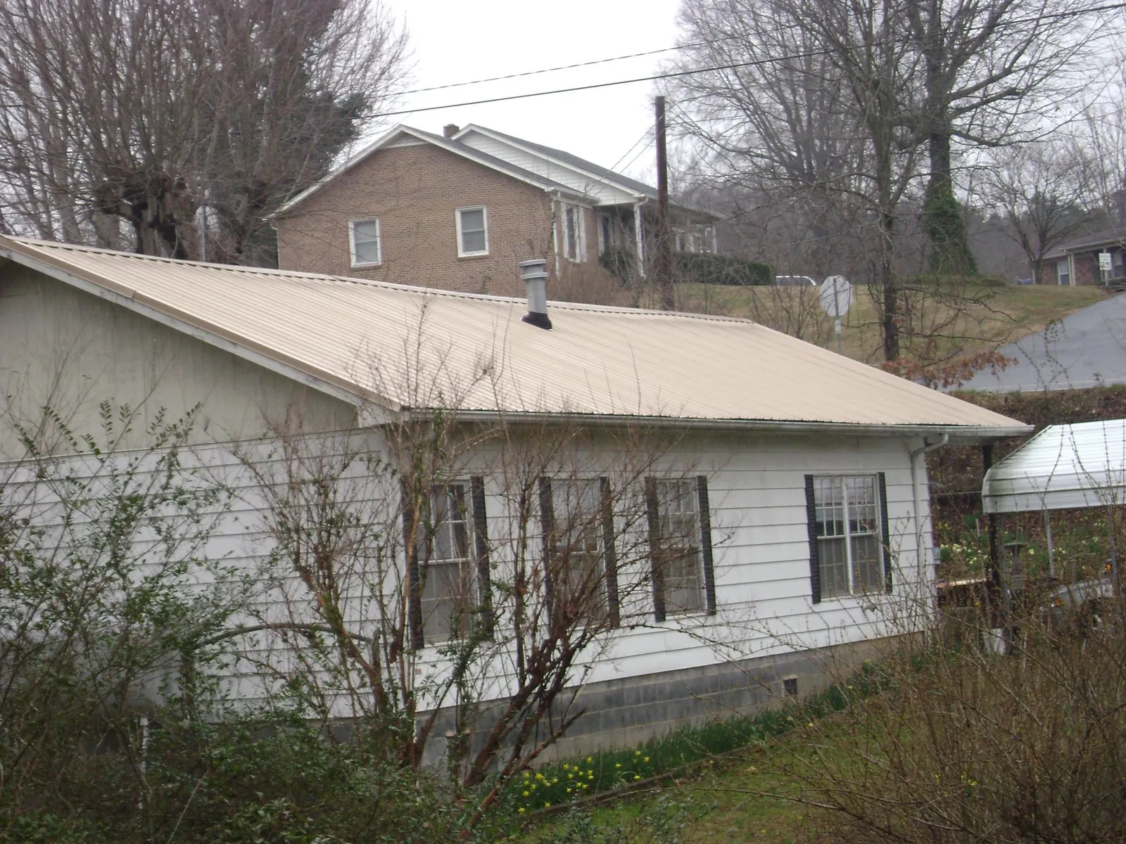 Tan metal roof on a white sided house set into a hillside — Commercial Roofing by Roofing Brothers in Brockton